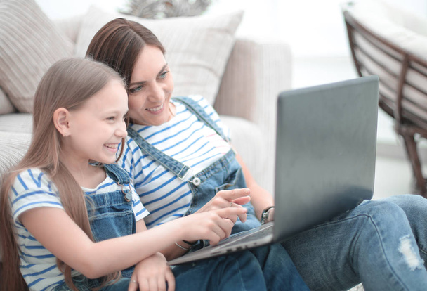 mamá y su hija sentadas en la alfombra en la sala de estar y utilizando un ordenador portátil - Foto, Imagen