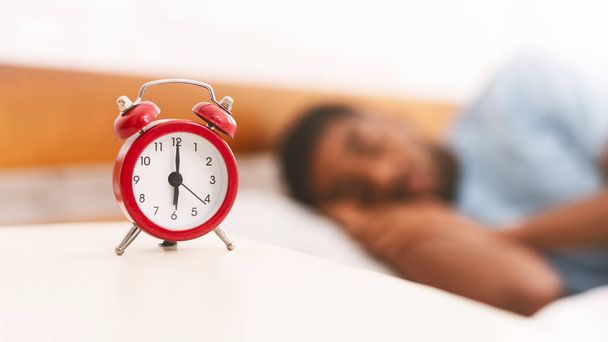 Homem dormindo com despertador em primeiro plano
 - Foto, Imagem