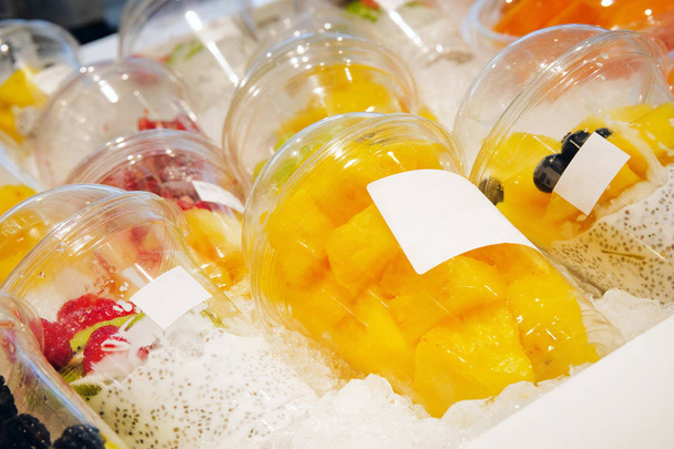 Pieces of pineapple and other fruits with chia seed yoghurt are laid out in plastic disposable cups and sold in store. Healthy vegetarian foods concept. Close up. - Photo, Image