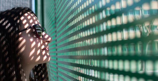 Portret van een meisje, een model in de buurt van een venster waarin zonlicht doordringt en laat prachtige patronen op haar gezicht. Mode, stijl, schoonheid, portret. - Foto, afbeelding