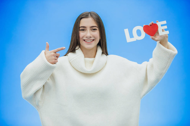 Young pretty girl dressed in white clothes. During this time it stands on a blue background. Holds a word of love in hands. - Photo, image