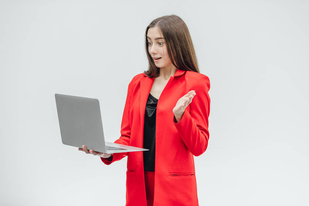 The image of a young business lady. Isolated on a gray background. Is worth it Using a gray laptop. Dressed in a red jacket. - Zdjęcie, obraz