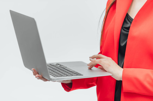 The image of a young business lady. Isolated on a gray background. Is worth it Using a gray laptop. Dressed in a red jacket. - Foto, afbeelding