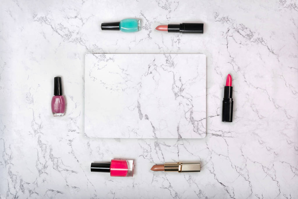 Frame made of various makeup products, lipstick and nail varnish with marble card on white marble texture - Foto, Imagem