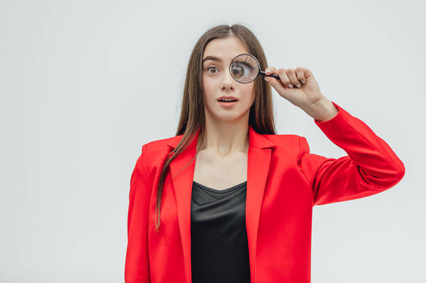 Funny expressions. Shocked woman looking at magnifying glass. A surprised girl looks at opening the keys with big eyes through a magnifying glass, isolated on a white background. - Photo, Image