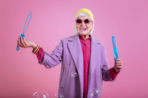シャボン玉で遊んで紫の服を着ている高齢者の女性 - 写真・画像