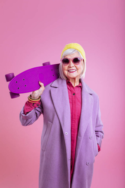 Modern beaming retired lady holding bright purple skateboard - Fotografie, Obrázek