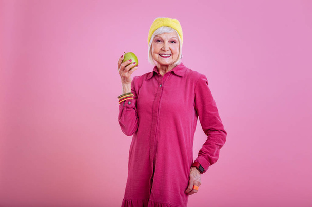 Retired lady wearing pink dress and head band holding apple - Photo, image