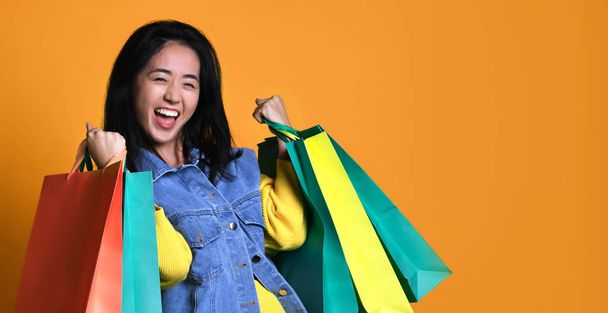 Young asian woman with shopping bags on color background - Foto, Imagem