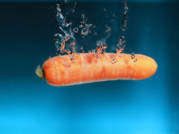 Carrot in the water splash over blue - Photo, image