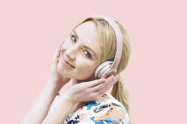 Edessä näkymä nuori valkoihoinen tyttö kuulokkeet ja kuunnella musiikkia vaaleanpunainen tausta
 - Valokuva, kuva