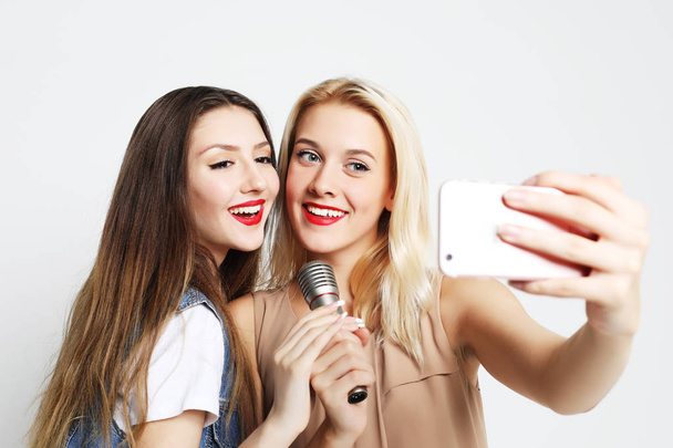 two beauty  girls with a microphone take selfie with smartphone  - Fotó, kép
