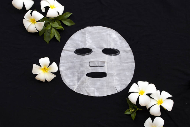 hyaluronová rostlinného aroma přírodní kosmetiky sítě list maska zdravotní péče o kůži obličeje extrakt z květu frangipani esence Obličejová maska na černém pozadí  - Fotografie, Obrázek