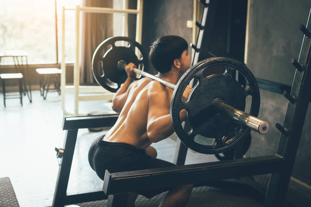 Asian man performing barbell squats at the indoor gym. - Фото, изображение