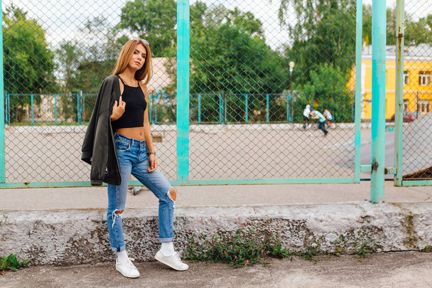 Fashion portrait of trendy young woman wearing sunglasses, jeans with halls and bomber jacket in the city - Фото, зображення