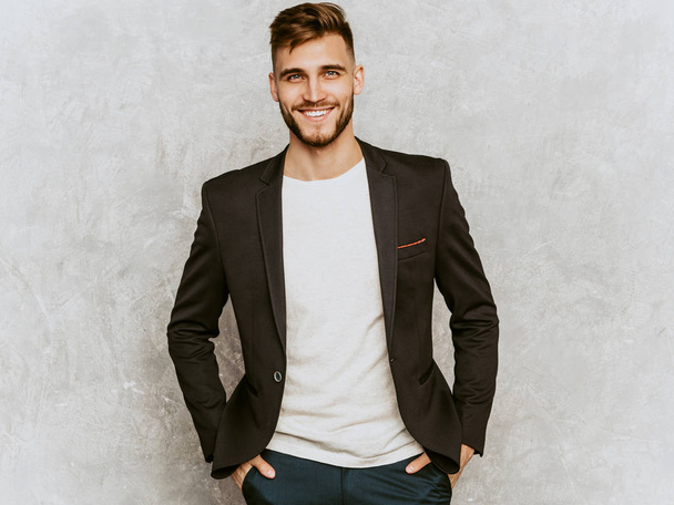 Portrait of handsome smiling hipster lumbersexual businessman model wearing casual black suit. Fashion stylish man posing against gray wall - 写真・画像