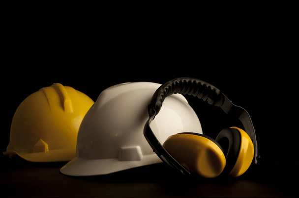 Gelbe Ohrenschützer aus Leder und Helme auf schwarzem Hintergrund. - Foto, Bild