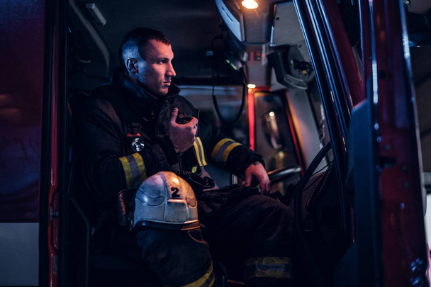 Η πυροσβεστική έφτασε στο της νύχτας. Πυροσβέστης κάθεται στο φωτιά φορτηγό και μιλώντας στο ραδιόφωνο - Φωτογραφία, εικόνα
