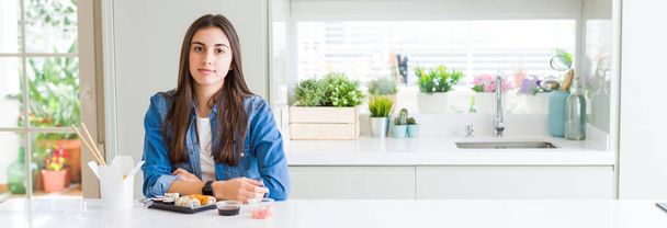 Wide angle picture of beautiful young woman eating delivery sushi with serious expression on face. Simple and natural looking at the camera. - Φωτογραφία, εικόνα