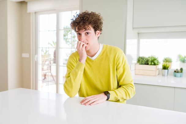 Fiatal jóképű férfi viselt sárga pulóver otthon látszó hangsúlyozni, és ideges, kezét, száját, harapós körmök. Szorongás a probléma. - Fotó, kép