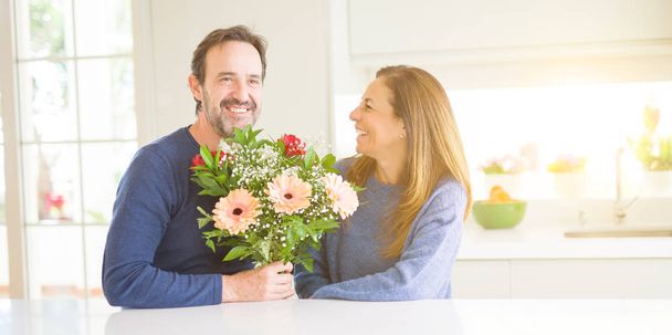 Couple romantique d'âge moyen tenant des fleurs en amour à la maison
 - Photo, image