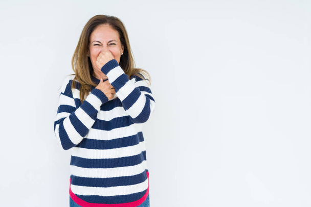 Beautiful middle age woman wearing navy sweater over isolated background smelling something stinky and disgusting, intolerable smell, holding breath with fingers on nose. Bad smells concept. - Photo, Image