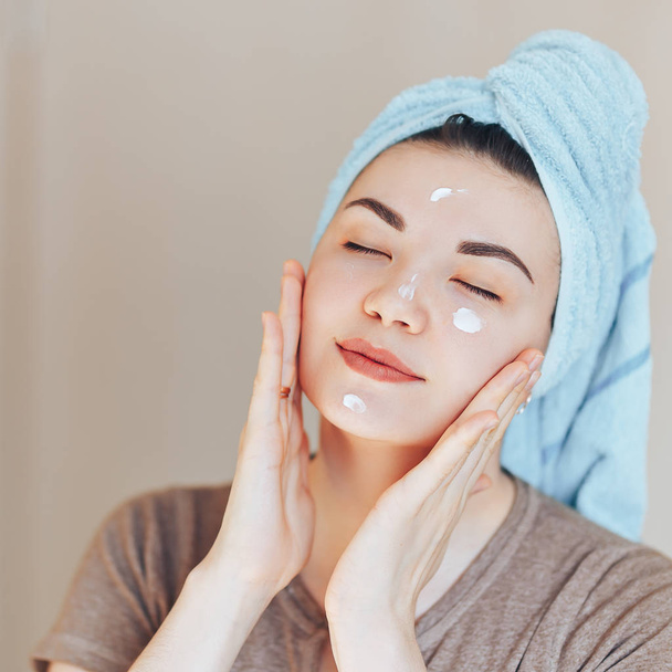 glücklich lächelnd hübsche Frau Mädchen mit Handtuch auf dem Kopf lächelnd berühren gesunde saubere weiche feuchtigkeitsspendende Hautpflege nach dem Auftragen von Creme auf das junge Gesicht - Foto, Bild