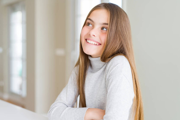 Szép fiatal lány gyerek mosolyogva látszó oldalon, és bámult el gondolkodás magas nyakú pulóvert visel. - Fotó, kép