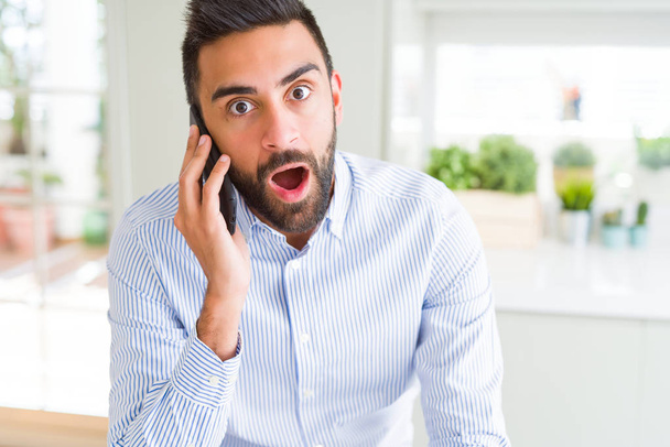 Pohledný Hispánská obchodní muž konverzaci mluví o smartphone strach v šoku s tváří překvapení, strach a vzrušený výraz strachu - Fotografie, Obrázek
