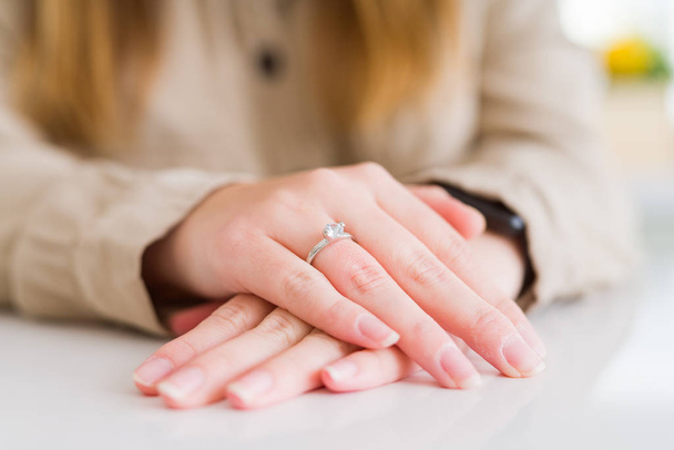 Primo piano del dito della donna che mostra anello di fidanzamento con le mani l'una sull'altra sul tavolo bianco
 - Foto, immagini