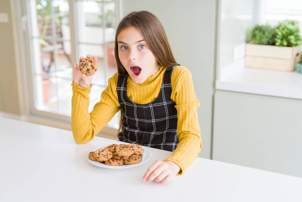 Belle jeune fille enfant mangeant des biscuits aux pépites de chocolat effrayé en état de choc avec un visage surprise, effrayé et excité par l'expression de la peur
 - Photo, image