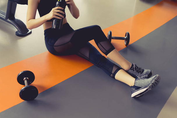 Nainen liikunta kuntosalilla kunto rikkomatta rentoutua harjoittelun jälkeen urheilu käsipaino ja proteiini ravista pullo terveellistä elämäntapaa kehonrakennus
 - Valokuva, kuva