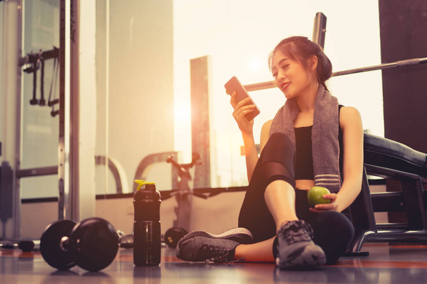 Relax nő gyakorlása edzés az edzőteremben fitness törés gazdaság Alma gyümölcs és használ smartphone után a képzés sport súlyzó és fehérje megráz üveg egészséges életmód testépítés. - Fotó, kép