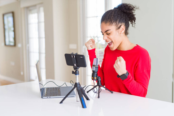 Young african american woman doing video call using smartphone camera and microphone very happy and excited doing winner gesture with arms raised, smiling and screaming for success. Celebration concept. - Photo, Image