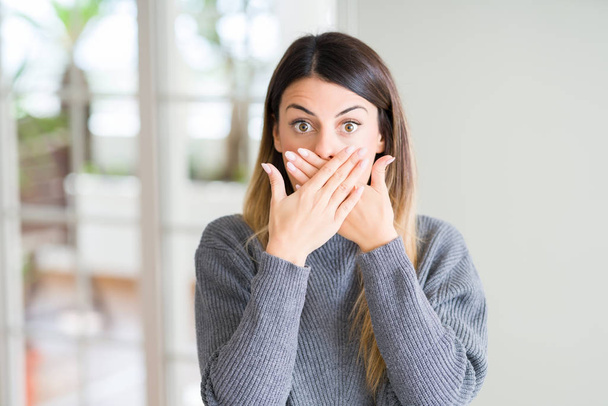 Young beautiful woman wearing winter sweater at home shocked covering mouth with hands for mistake. Secret concept. - Photo, Image