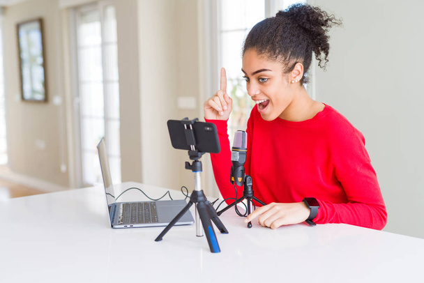 Young african american woman doing video call using smartphone camera and microphone pointing finger up with successful idea. Exited and happy. Number one. - Photo, Image