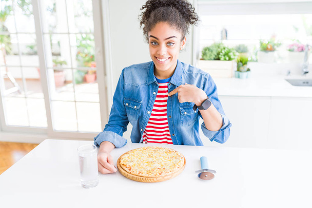 Mladá africká americká žena jíst pizzu domácí sýr s překvapením tvář ukazováčkem na sebe - Fotografie, Obrázek