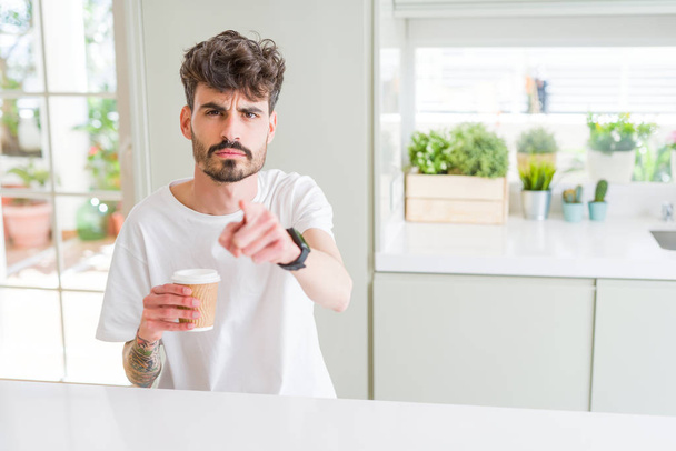 junger Mann, der morgens einen Kaffee in einer Papptasse trinkt und mit dem Finger auf die Kamera und Sie zeigt, Handzeichen, positive und selbstbewusste Geste von vorne - Foto, Bild