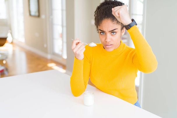 Nuori afrikkalainen amerikkalainen nainen syö terveellistä luonnollista jogurttia ärtynyt ja turhautunut huutaa vihaa, hullu ja huutaa kohotettu käsi, viha käsite
 - Valokuva, kuva