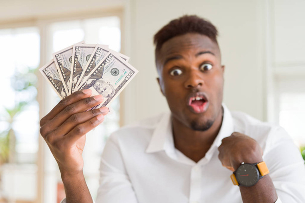African american man holding fifty dollars bank notes with surprise face pointing finger to himself - Фото, изображение