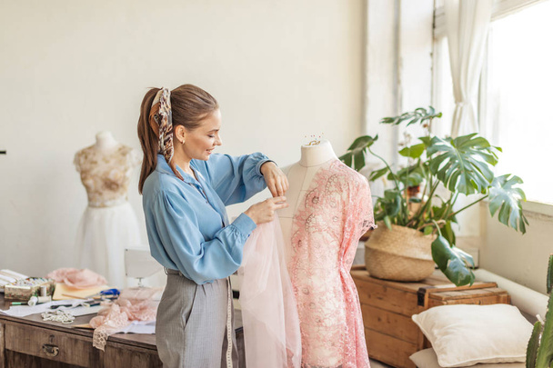 Beautiful seamstress is working with a wedding dress model in her studio - Foto, Imagen