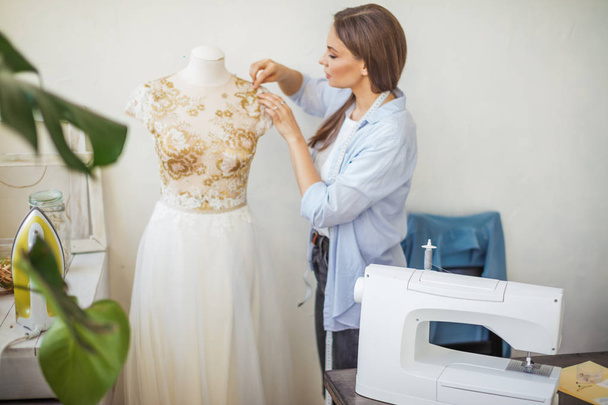 Beautiful seamstress is working with a wedding dress model in her studio - Photo, Image
