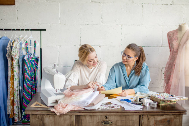 Female dressmaker showing design to her client, sitting together at workshop. - Foto, immagini