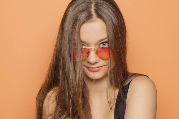 Νεαρό χαμογελαστό κορίτσι με τα πορτοκαλί γυαλιά ηλίου σε πορτοκαλί φόντο - Φωτογραφία, εικόνα
