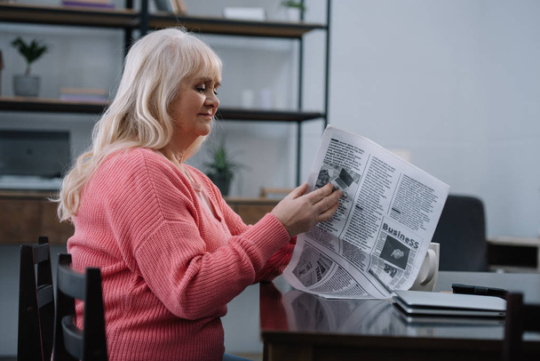 vezető nő ül az asztalnál, és az olvasás üzleti napilap otthon - Fotó, kép