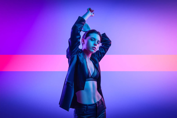 Cinematic night portrait of woman in  neon. High Fashion model girl in colorful bright neon lights posing in studio, portrait of beautiful woman in   jacket, underwear and trousers.  - Zdjęcie, obraz