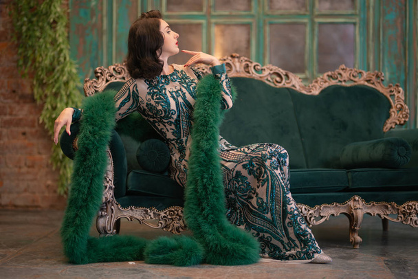 элегантная кавказская девушка в роскошных длинных блестках кружевное платье с зеленым пушистым боа в руках позирует в комнате ретро с старинной роскошной мебелью
 - Фото, изображение