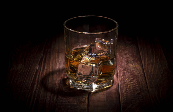 Sklenice whisky a některé kostky ledu na dřevěný stůl - Fotografie, Obrázek