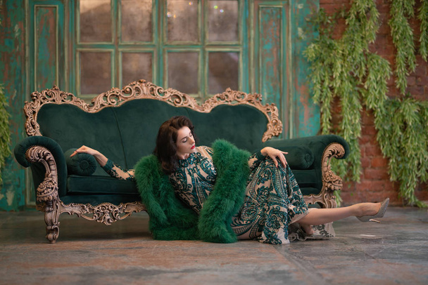 élégante fille caucasienne dans une robe de dentelle longue paillettes luxueuse avec un boa moelleux vert dans ses mains posant dans la chambre rétro avec des meubles de luxe vintage
 - Photo, image