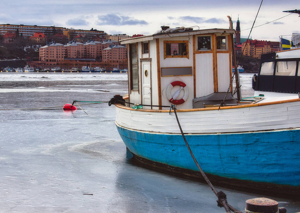 Small fishing boat with a blue hull moored on a frozen river in winter - Photo, Image